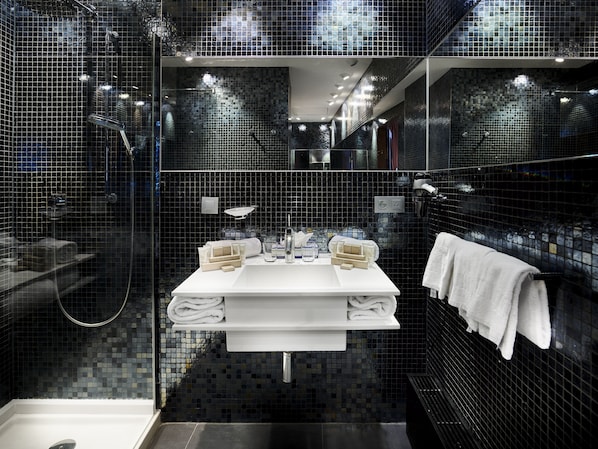 Un baño moderno con ducha envuelta en vidrio, un lavamanos blanco con dos senos y un espejo grande sobre el lavamanos.
