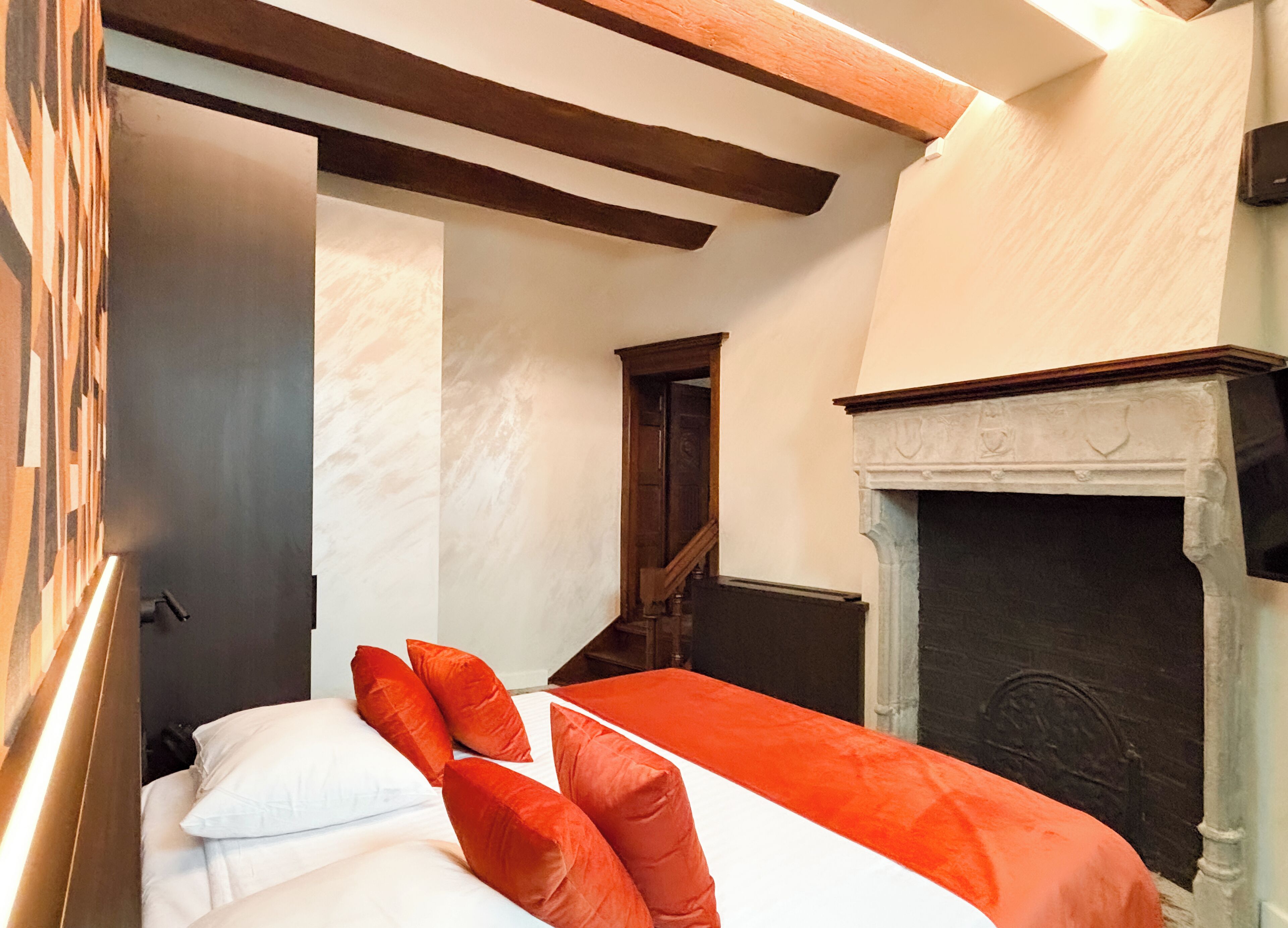 A bedroom with a bed, pillows, a fireplace, and a wooden ceiling.