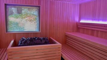 Un sauna con bancos de madera, una ventana con vista a la vegetación y un banco de piedra con rocas.