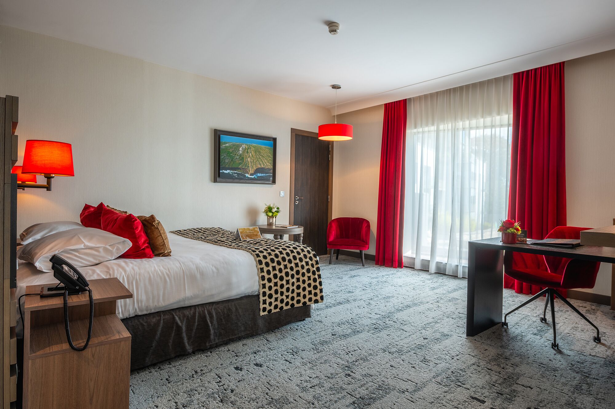 Une chambre d’hôtel avec un lit, un bureau, une chaise, une lampe et un tableau au mur.