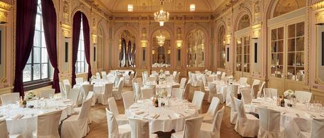 Un vaste hall de banquet orné de lustres somptueux, de nappes blanches et de chaises élégantes.