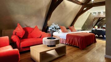 A cozy attic bedroom with a red sofa, a wooden coffee table, and a bed with red bedding.