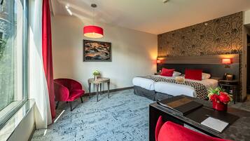 A hotel room with a bed, a desk, a chair, a small table, and a window with curtains.
