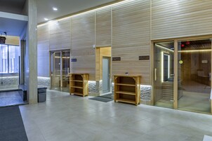 Un moderno vestíbulo de hotel con paneles de madera, una recepción y un área de sauna visible.