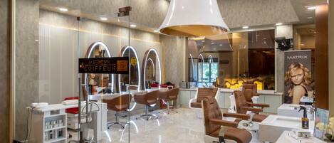 Interior moderno de salón con varias estaciones de peluquería, un letrero visible que dice 'La Stone Spa Coiffeur', y un espejo grande que refleja el interior del salón.