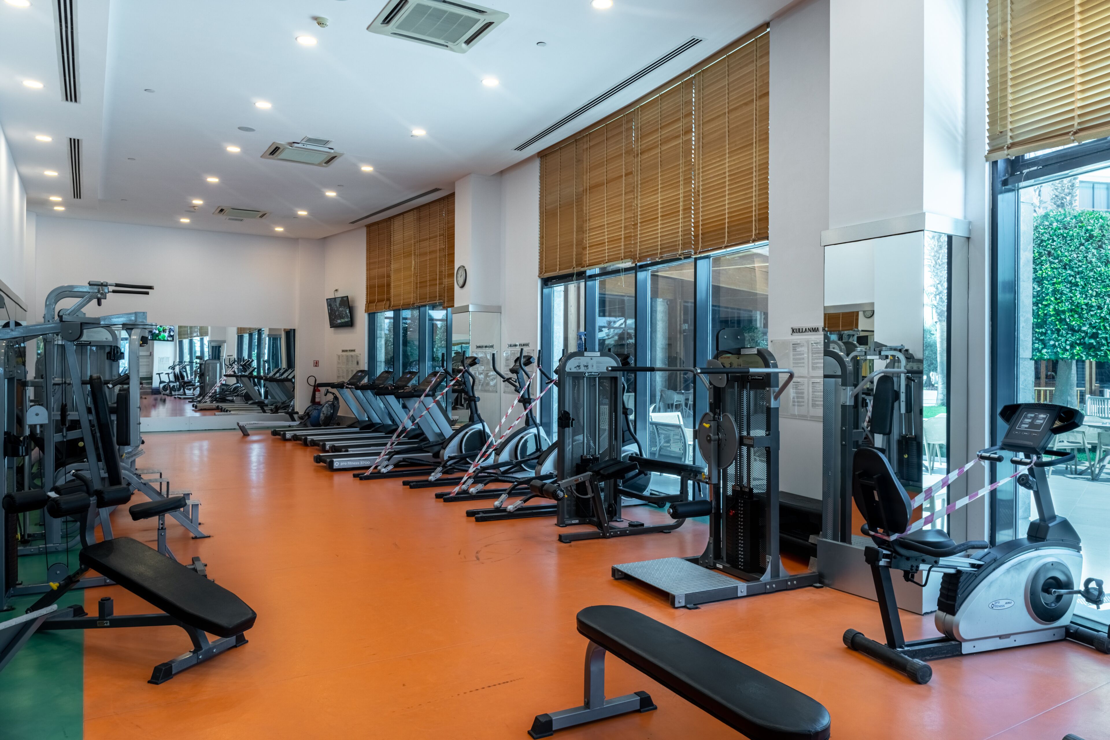 A gym with various exercise equipment, large windows, and a bright interior.