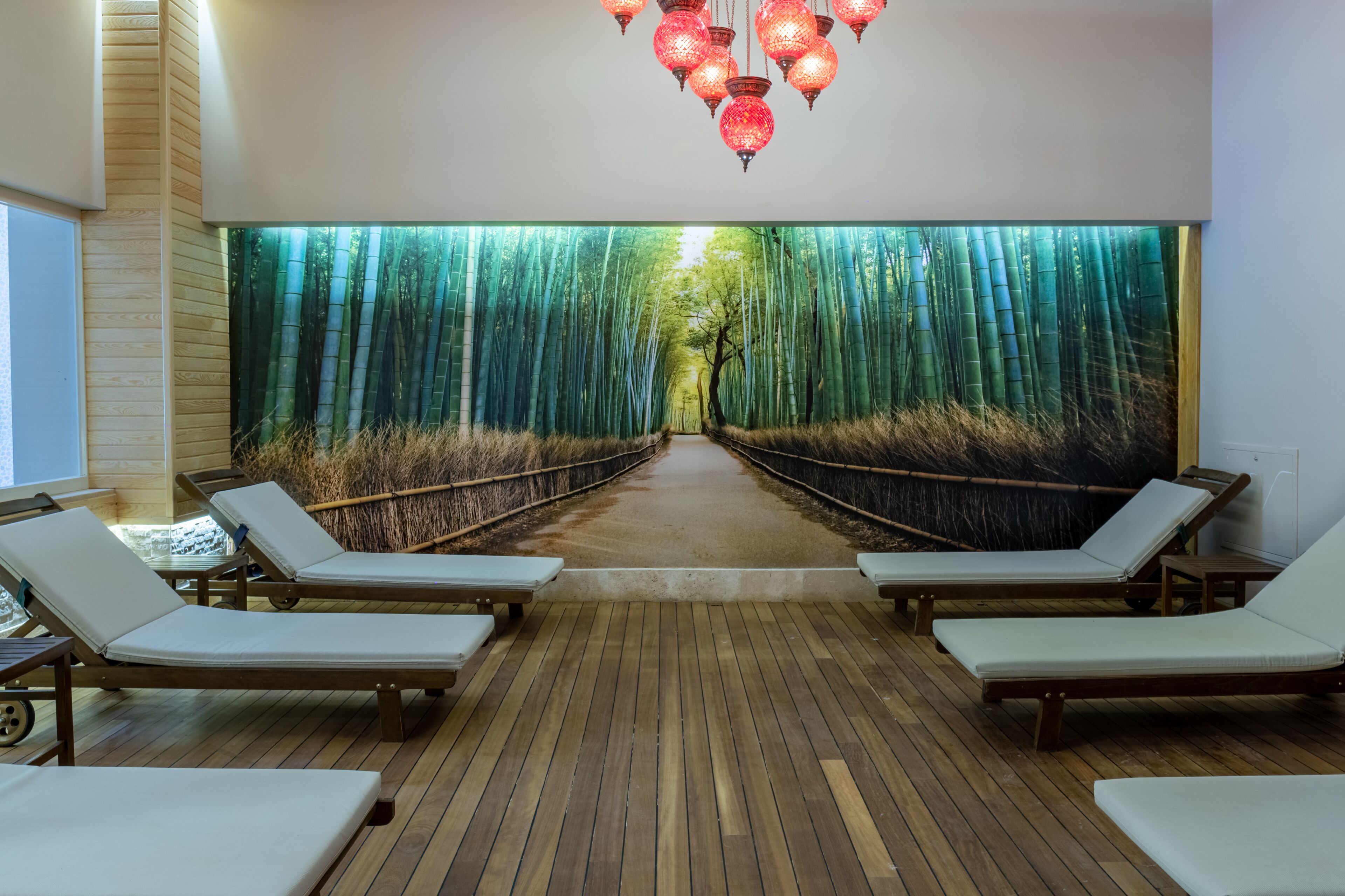 A spa area with wooden flooring, white lounge chairs, and a large wall mural of a bamboo forest.