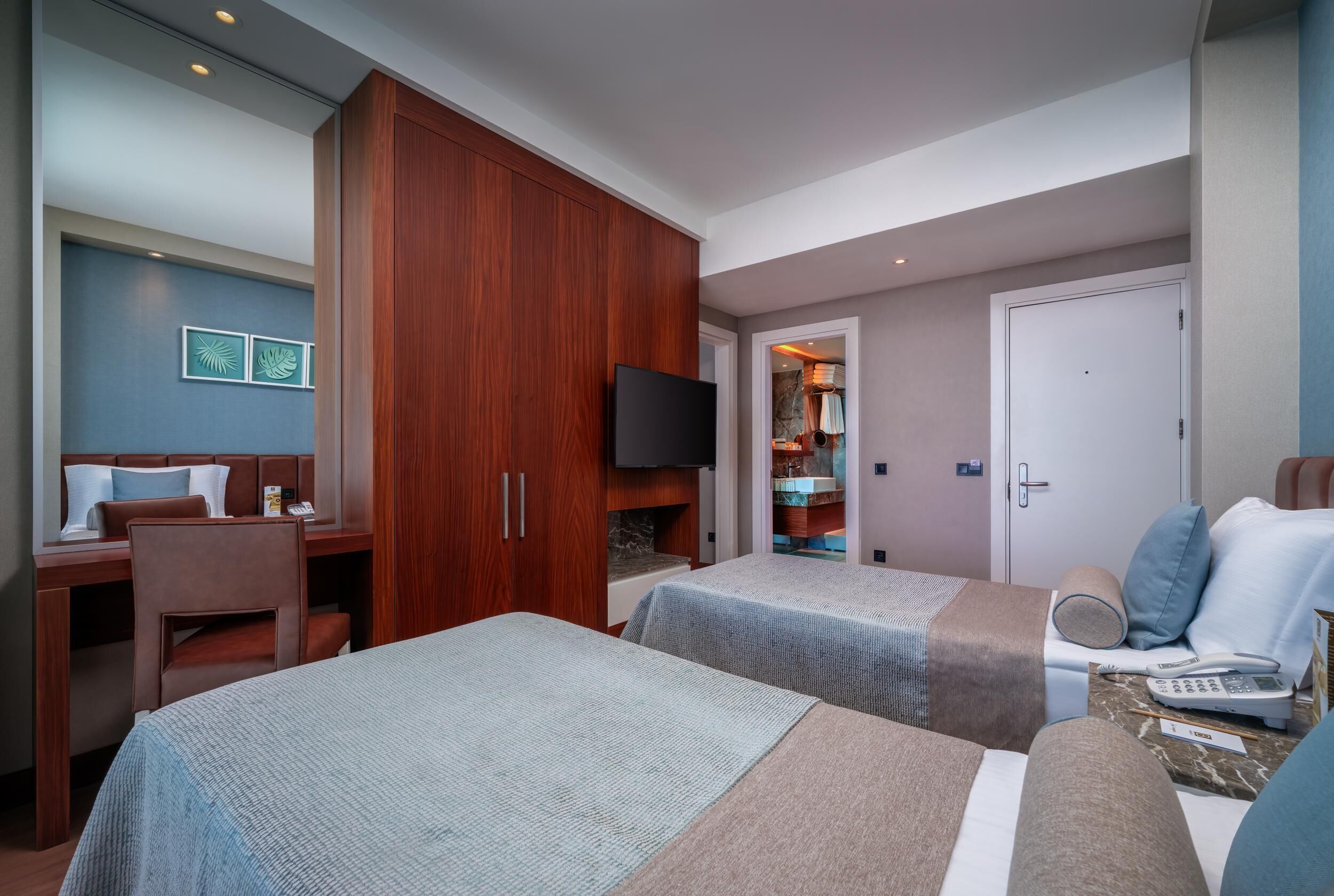 A hotel room with two beds, a desk, a TV, and a wardrobe.