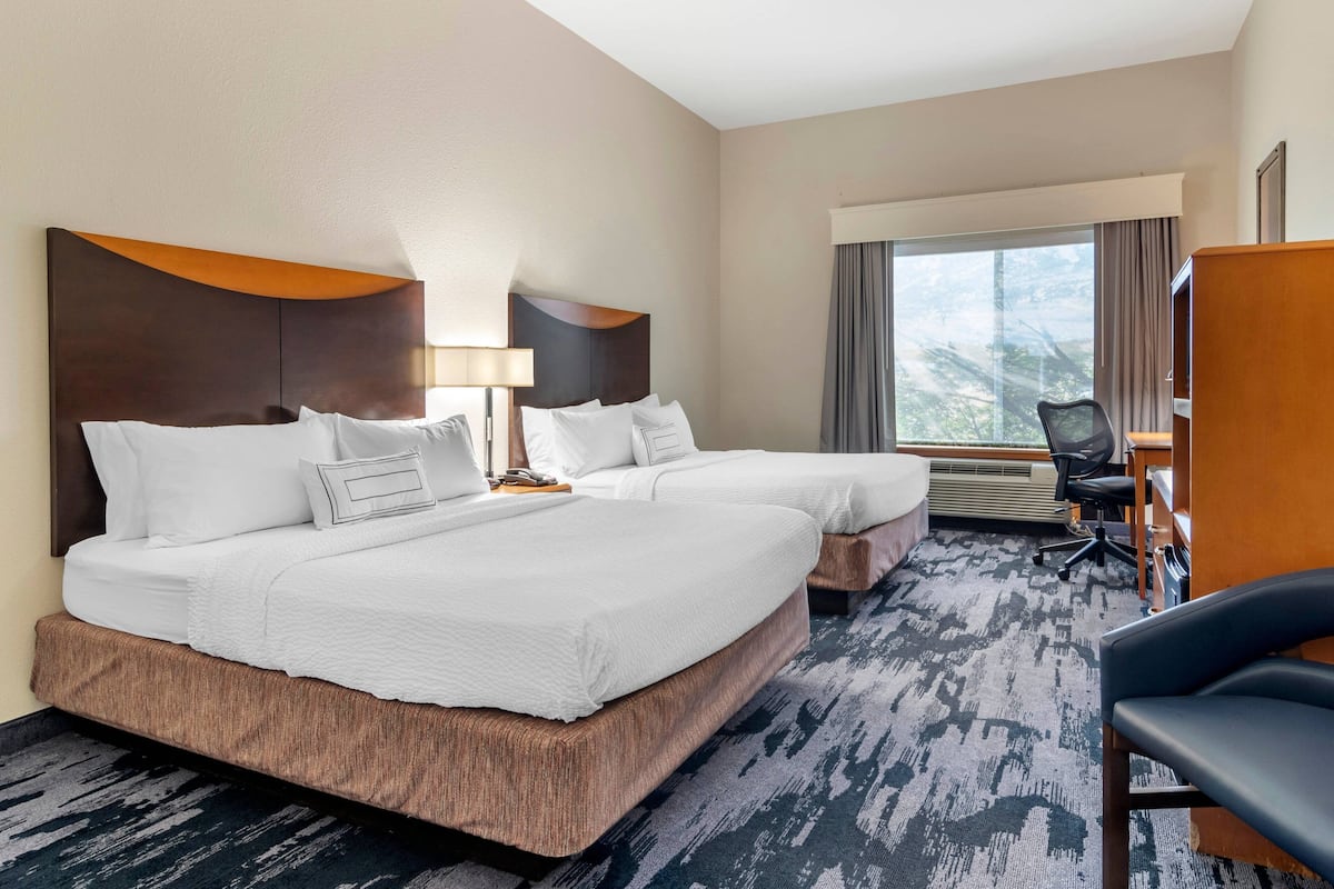 A hotel room with two beds, a desk, a chair, and a large window.
