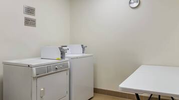 A laundry room with two washing machines, a table, and a clock on the wall.