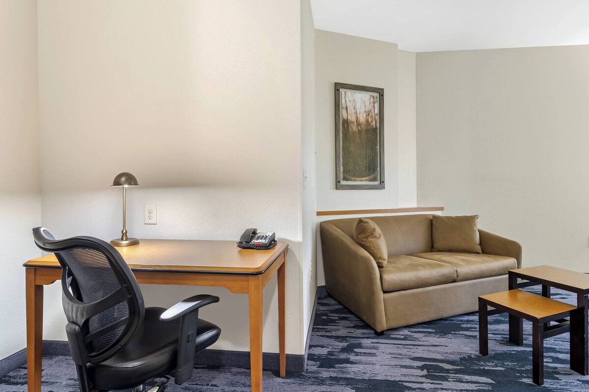 A hotel room with a desk, chair, and a sofa.