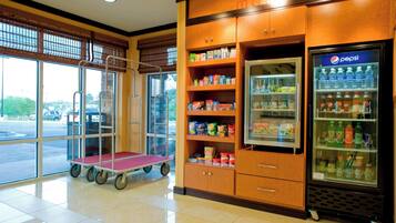 Zona de máquinas expendedoras con aperitivos y bebidas, un carrito y vistas al exterior.