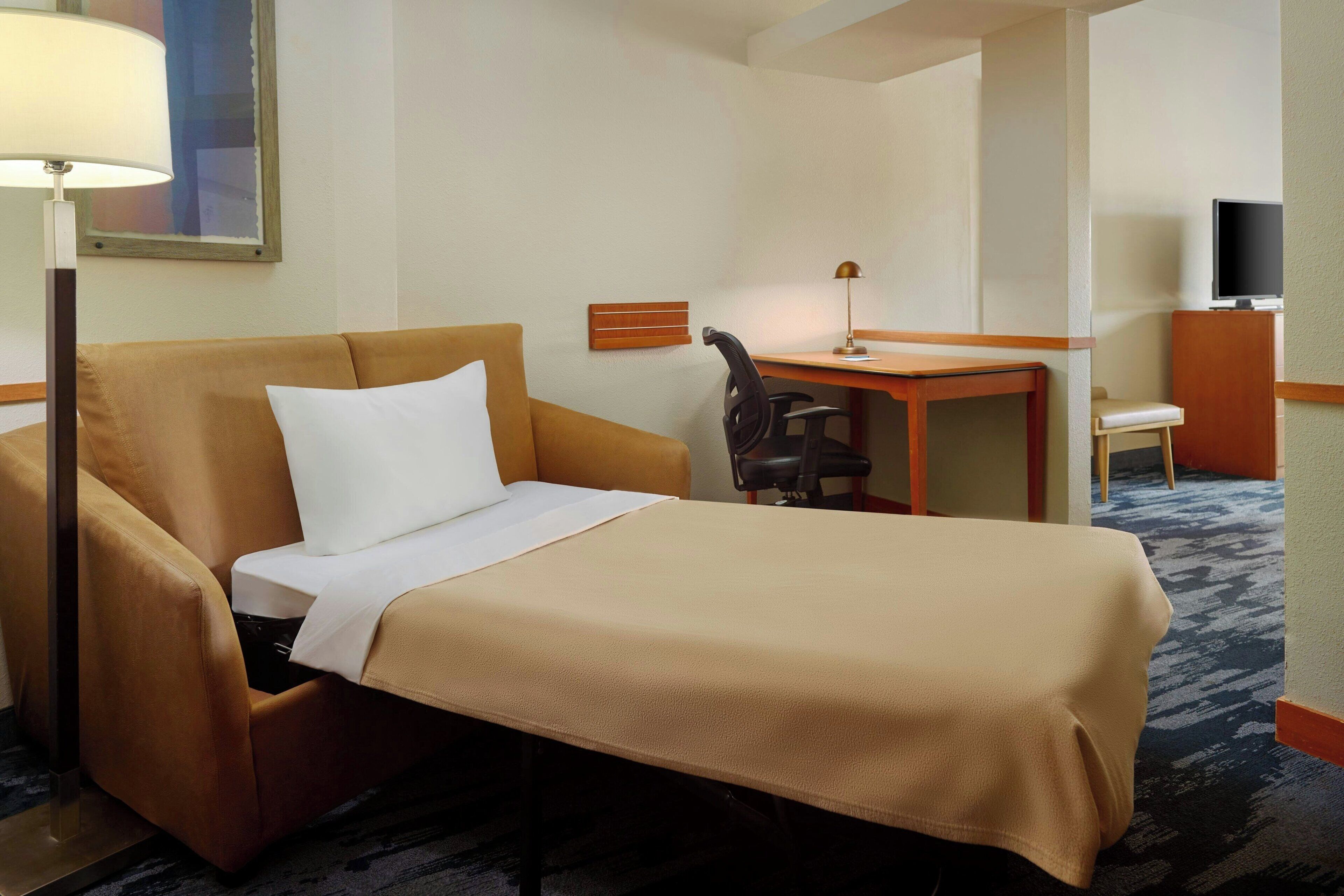 Una habitación de hotel con una cama individual, un escritorio, una silla y un televisor.