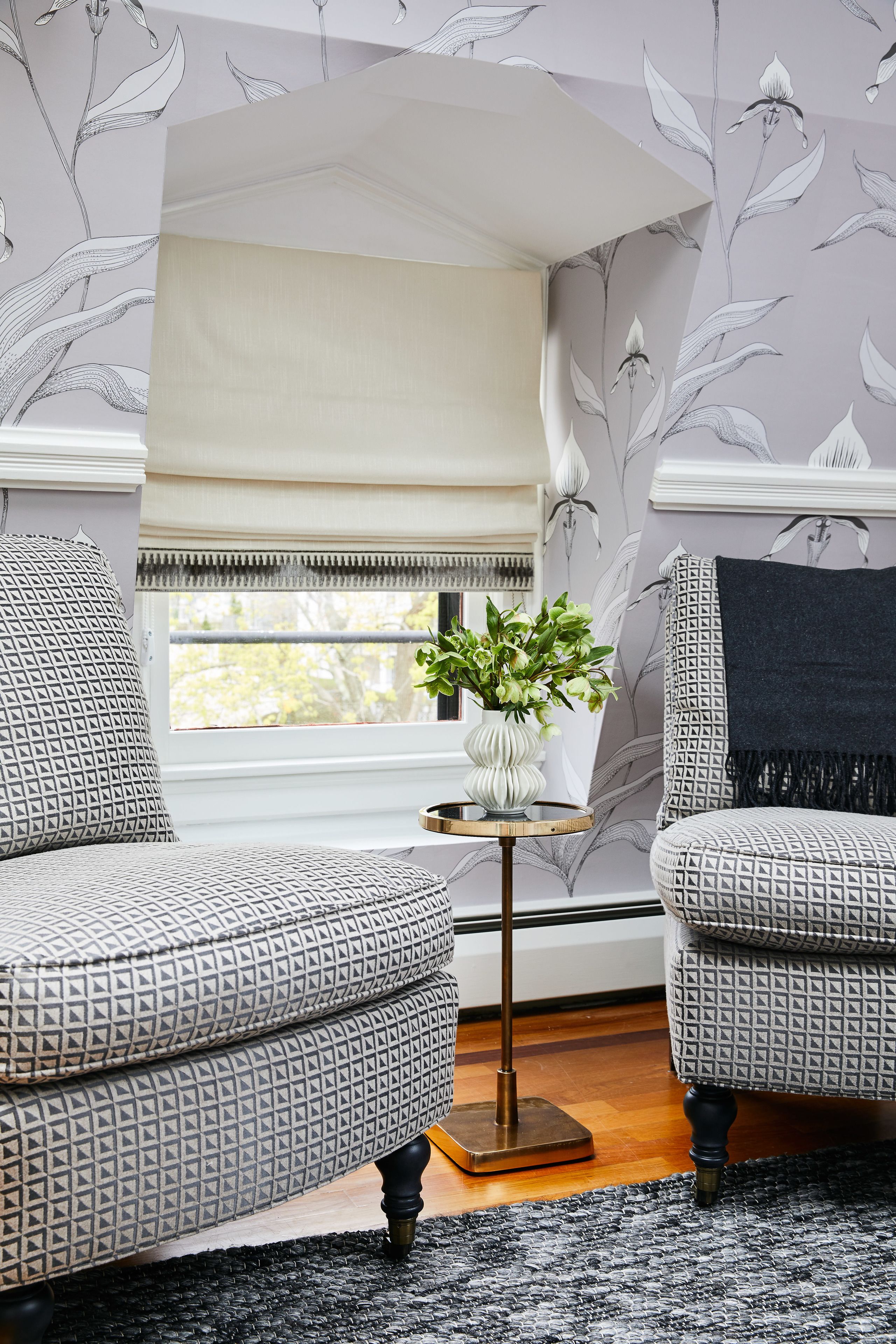 Een kamer met gestreept fauteuils, een tafeltje met een plant en een raam met een beige lambrisering.