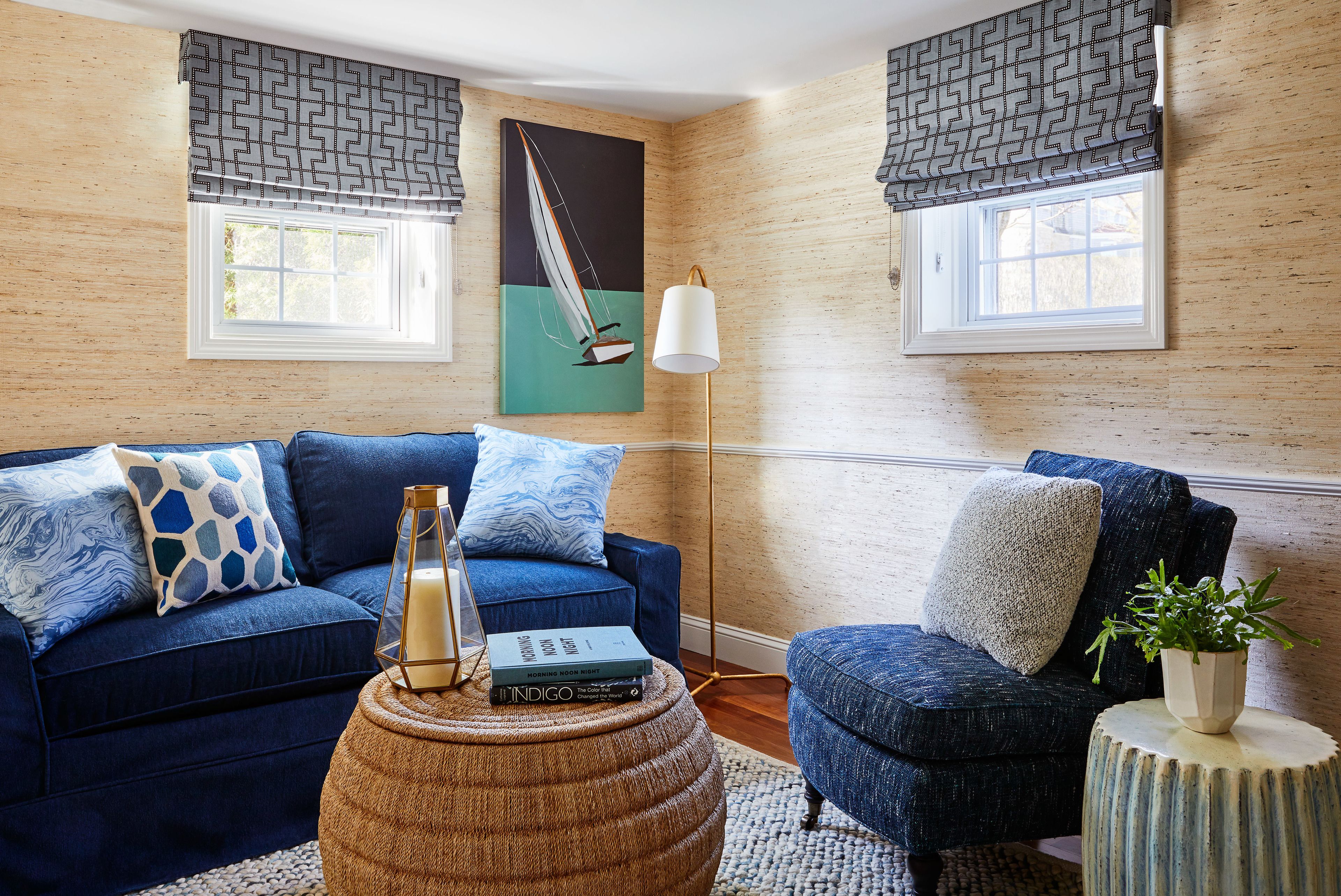 A living room with a blue sofa, a round ottoman, and a potted plant.
