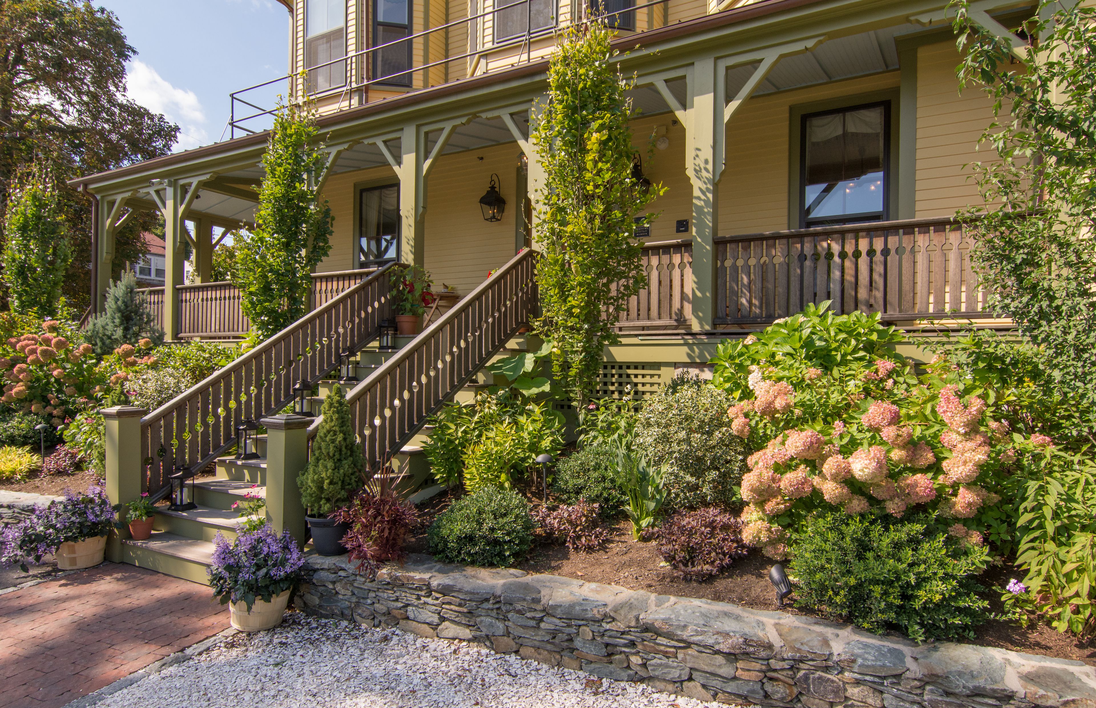 A two-story house with a front porch, a staircase, and a garden with various plants and flowers.