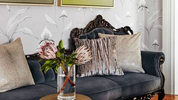 Ein dunkelblaues Sofa mit dekorativer Kopfteil, ein runder Tisch mit Blumenvase und floraler Wandtapete.