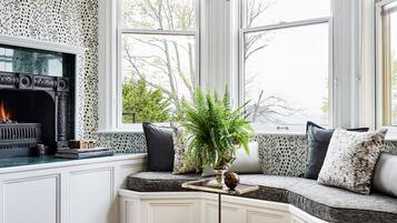 A cozy room with a fireplace, a bench with cushions, a potted plant, and a unique patterned wall.