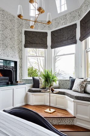 A cozy room with a fireplace, a bench with cushions, a potted plant, and a unique patterned wall.