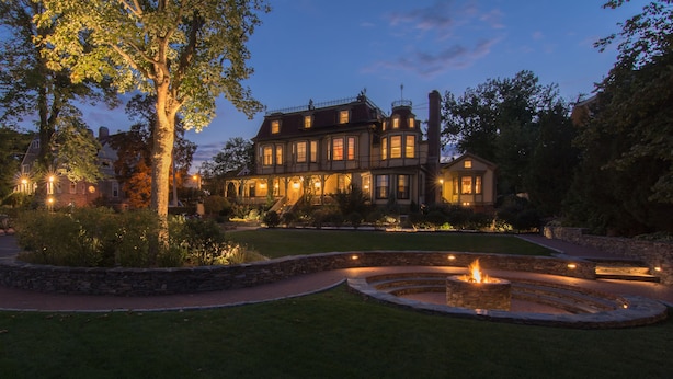 Una casa grande e histórica con un jardín cuidado y una chimenea central.