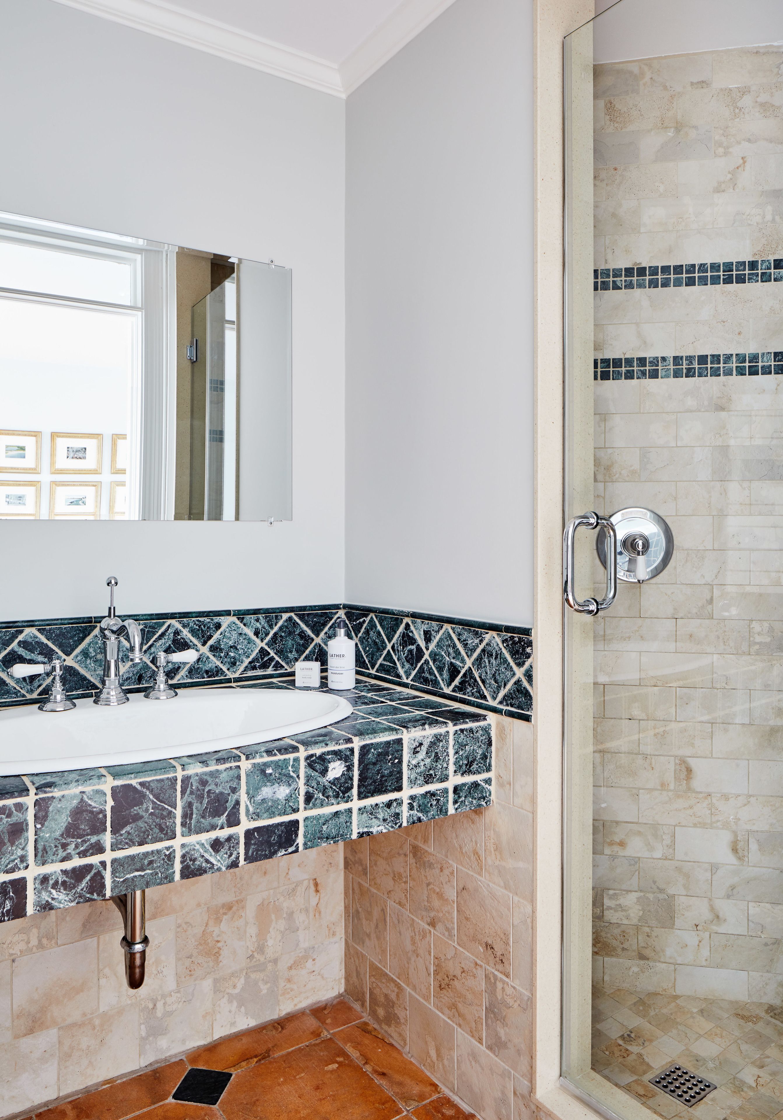 A bathroom with a sink, mirror, and shower area.