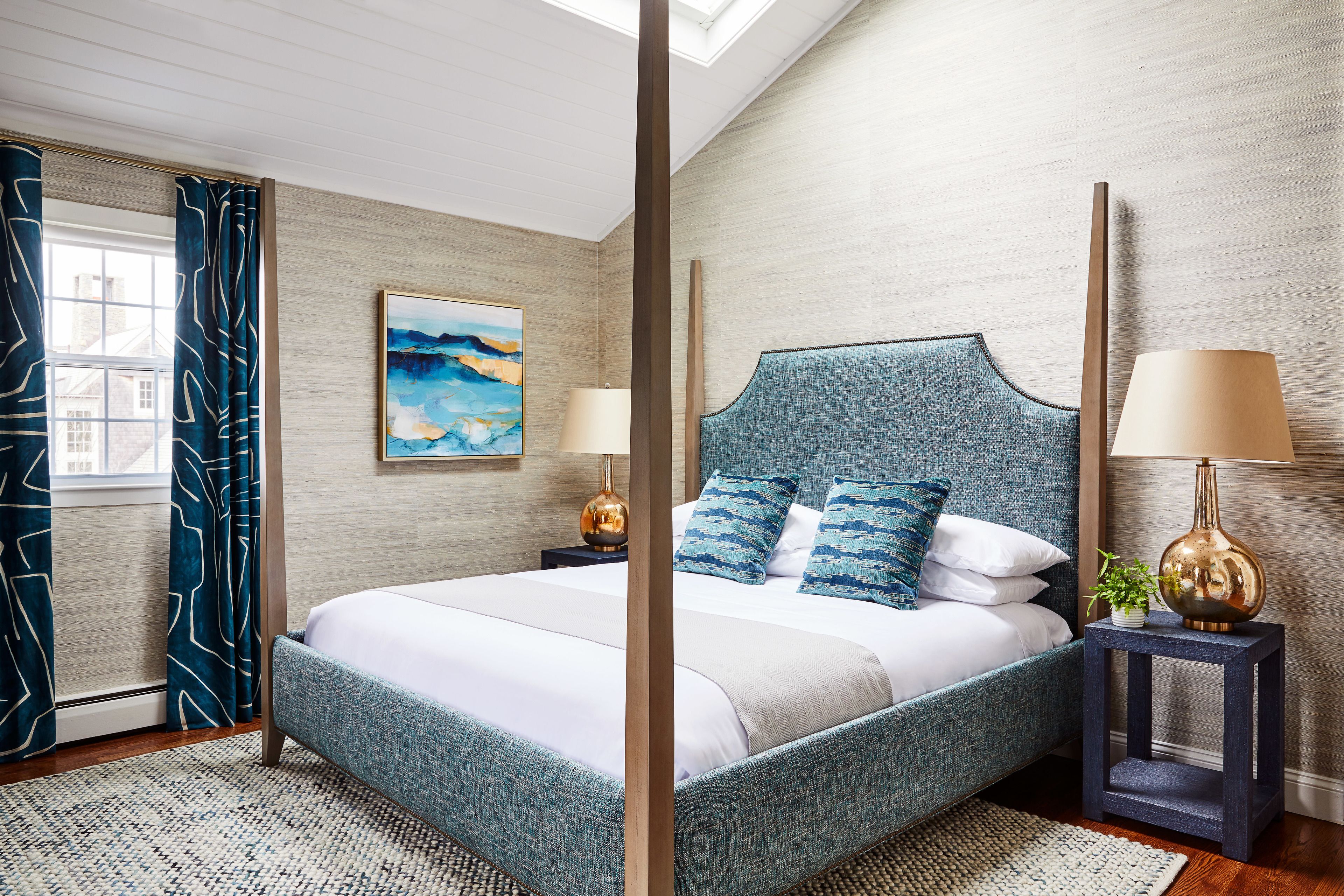 Une chambre moderne avec un grand lit, deux tables de chevet avec des lampes, un tableau au mur et une vue sur l’extérieur par une fenêtre avec des rideaux.