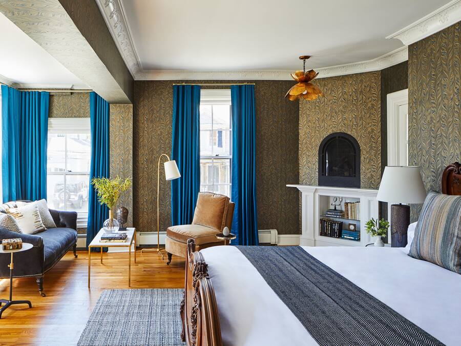 A hotel room with a large bed, a sofa, a chair, a small table, and a fireplace.