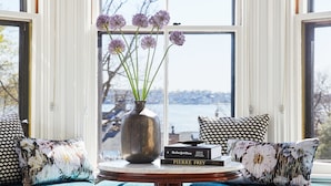 Un ventanal con vistas a una masa de agua, un jarrón con flores y un libro titulado "PIERRE FREY" sobre una mesa.