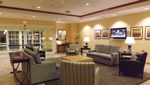 A hotel lobby with a seating area, a television, and a desk with a lamp.