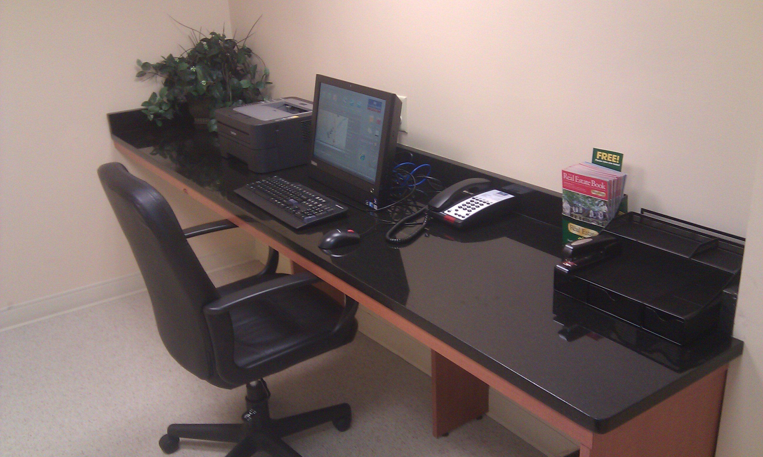 A desk with a laptop, a desktop computer, a telephone, and a book on real estate.
