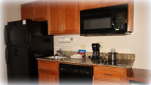 A kitchen with wooden cabinets, a black refrigerator, a microwave, a coffee maker, and a dishwasher. - Candlewood Suites Fredericksburg by IHG (Fredericksburg)
