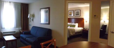 A hotel room with a bed, a sofa, a dining table, and a chair.