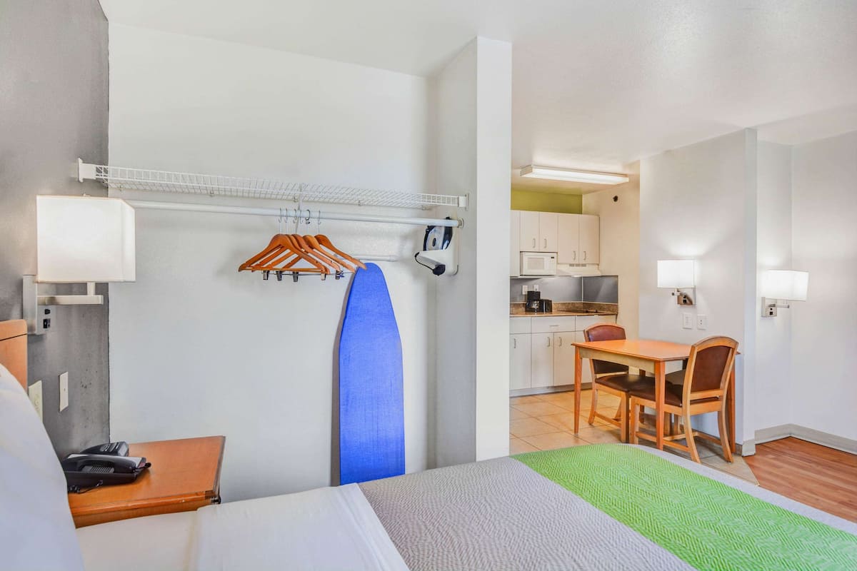 Quarto de hotel com cama, escrivaninha, cadeira, mesa de jantar, cozinha e um varal.
