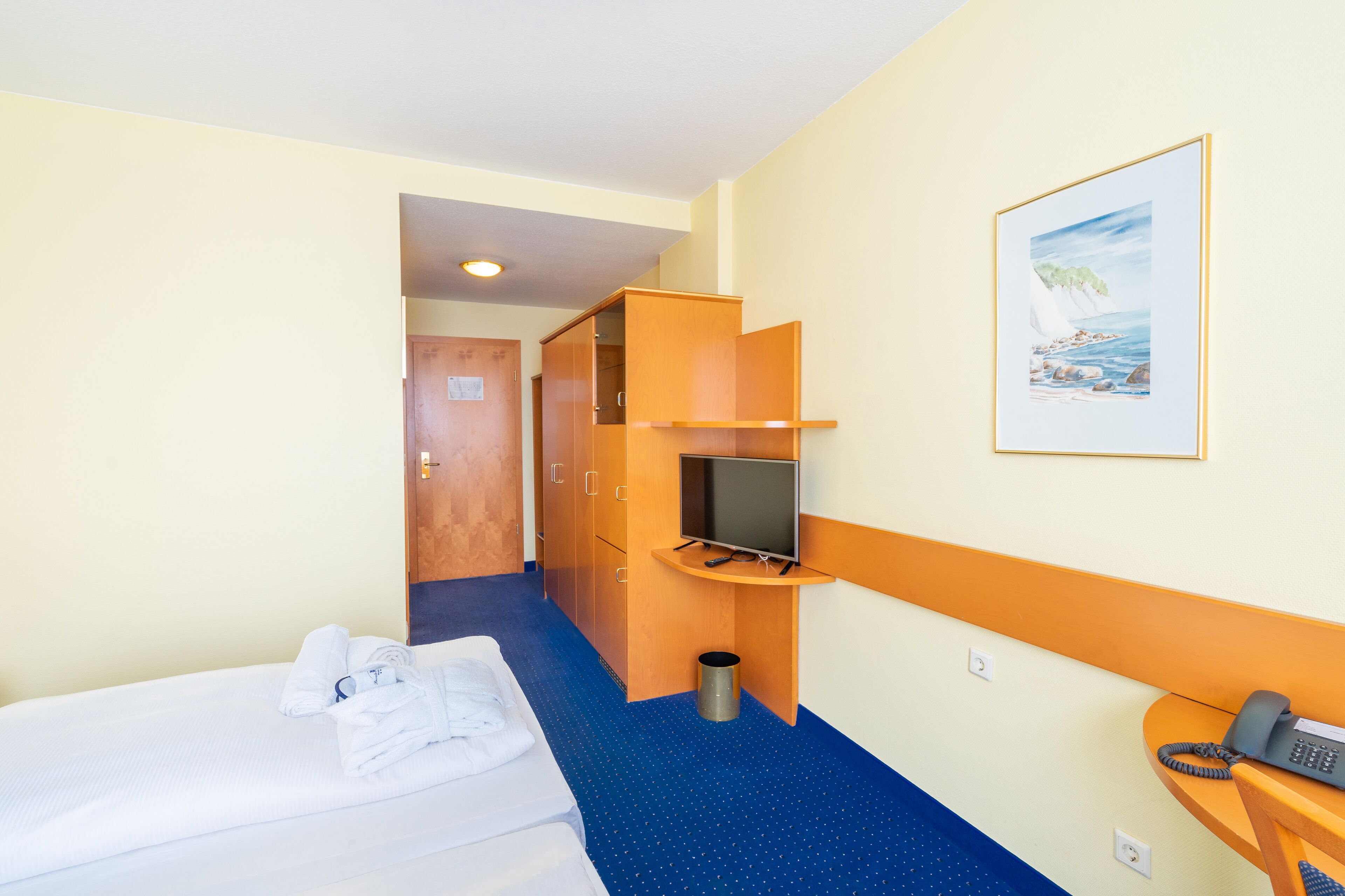 A hotel room with a bed, a television, a desk with a phone, and a painting on the wall.