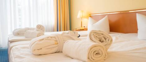 A neatly made bed with rolled towels, a bedside lamp, and a framed picture on the wall.