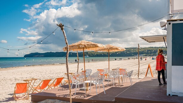 Un área de estar frente a la playa con sombrillas y sillas, con vista al mar.