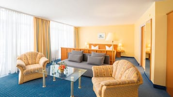 A hotel room with a sofa, two armchairs, a glass coffee table, and a lamp.