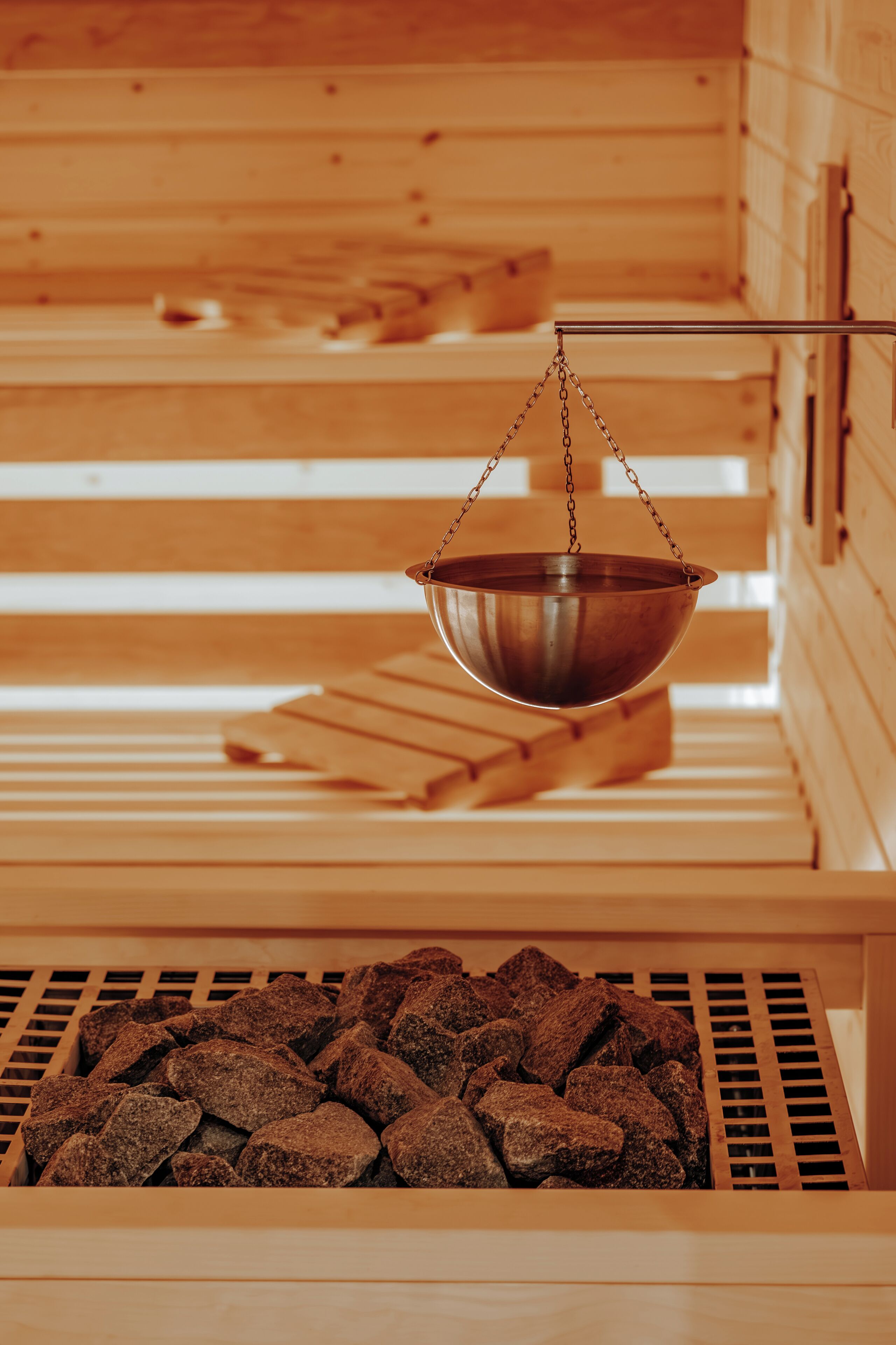 A sauna with wooden benches and a metal basin hanging from the ceiling.