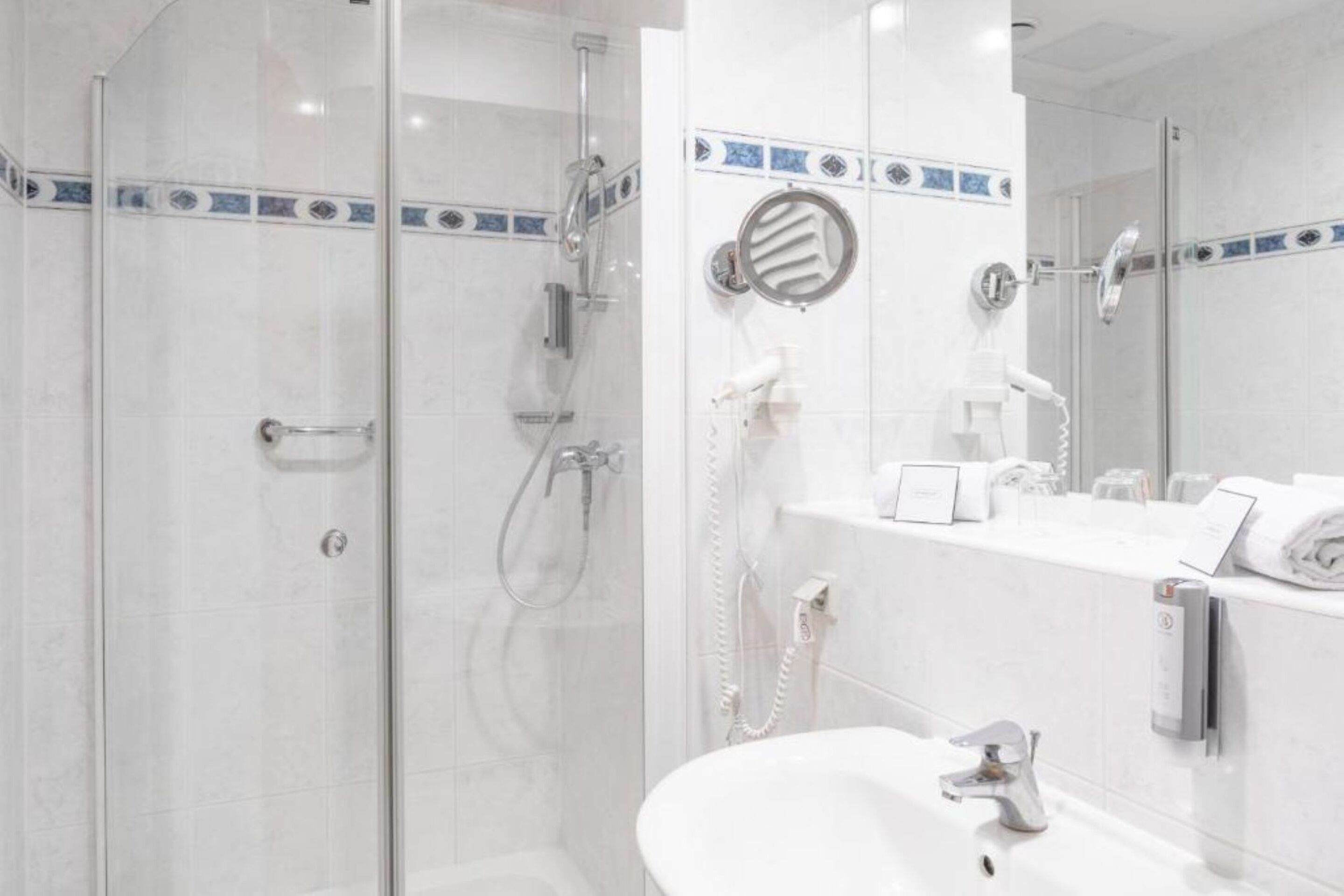 A modern bathroom with a glass-enclosed shower, a white sink, and a mirror with a towel rack.