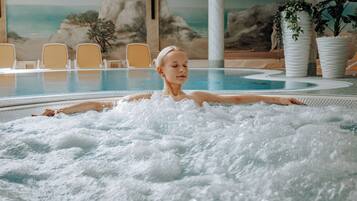 A person relaxing in a hot tub with a mural of a beach and chairs in the background.
