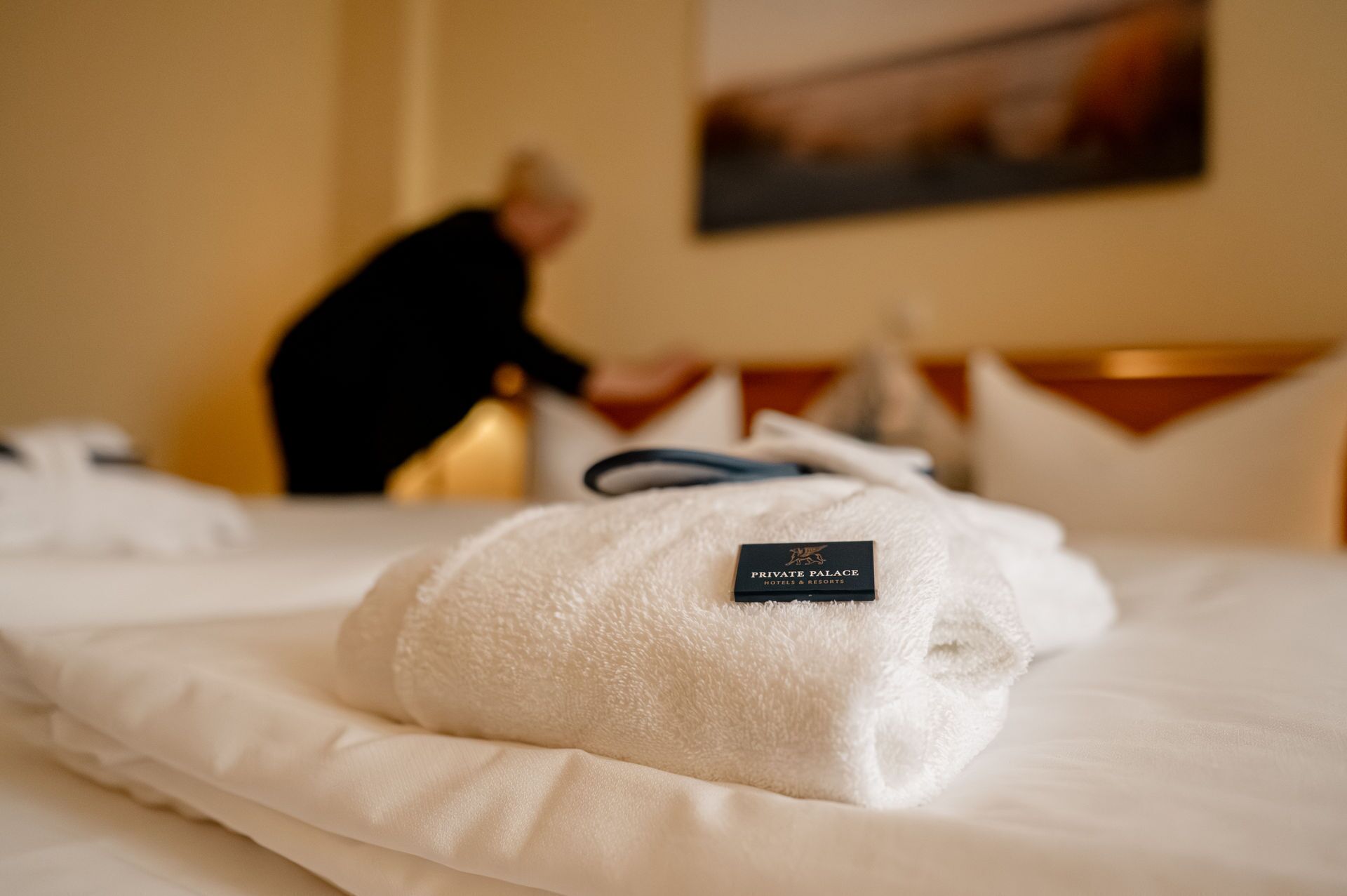 A neatly made bed with a towel and a tag labeled "PRIVATE PALACE HOTELS & RESORTS" in a hotel room.