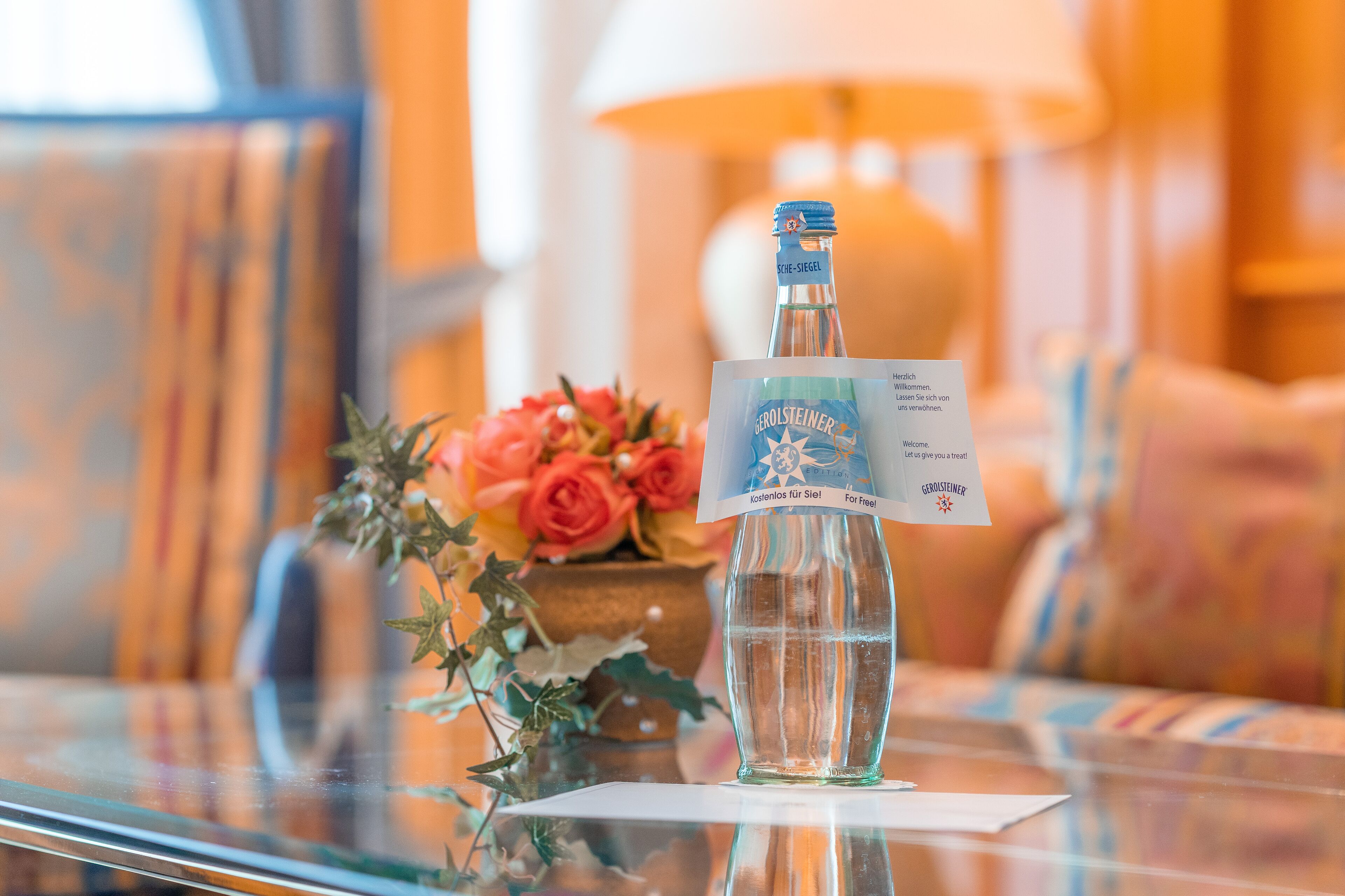 Een fles Gerolsteiner bier op een glazen tafel met een kaartje en een bloemenboeket.