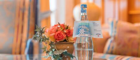 A bottle of Gerolsteiner beer on a glass table with a card and a bouquet of flowers.