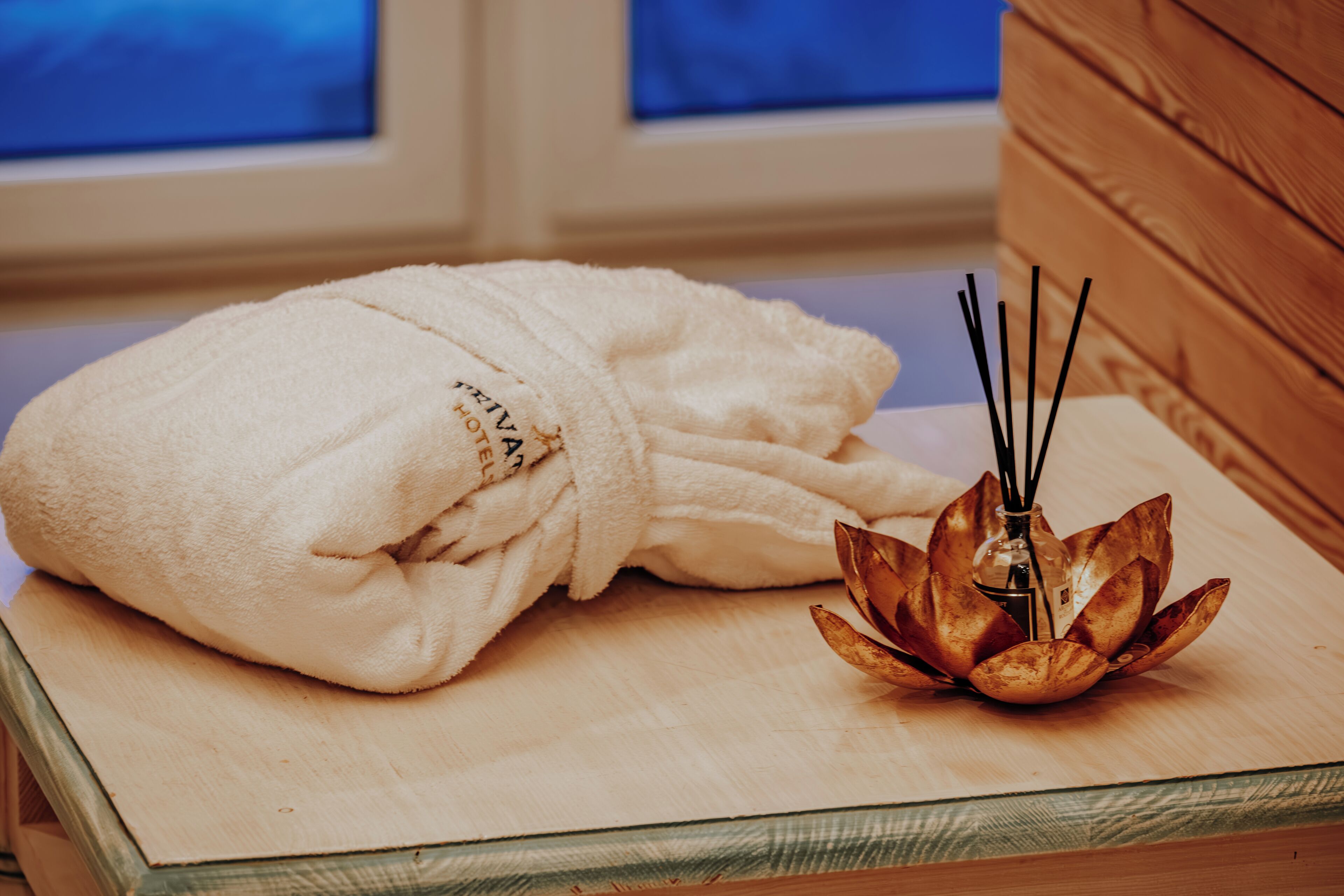 A white bathrobe on a wooden tray with a decorative lotus-shaped candle holder.