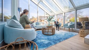 Una habitación amplia con un gran techo de vidrio, un sofá azul claro, una mesa de centro de mimbre y una alfombra azul.