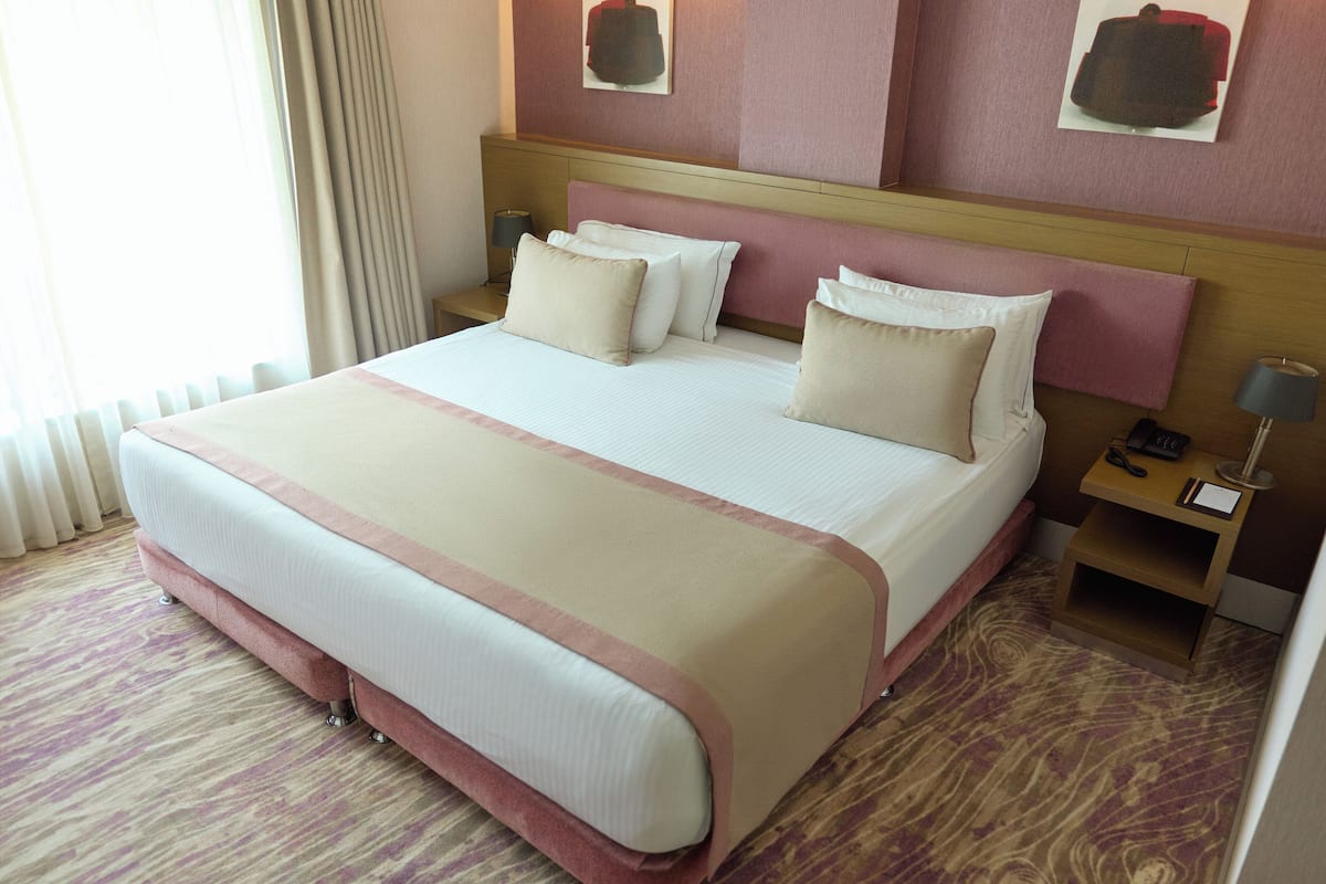 A hotel room with a large bed, a wooden headboard, and a nightstand with a lamp.