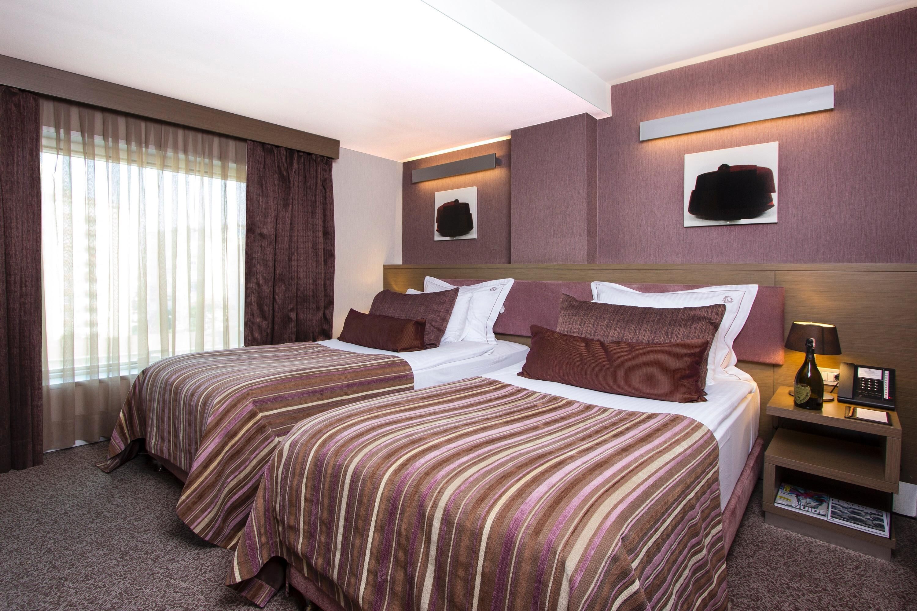 Een hotelkamer met twee bedden, een nachtkastje met een lamp, een fles champagne en kunst aan de muren.
