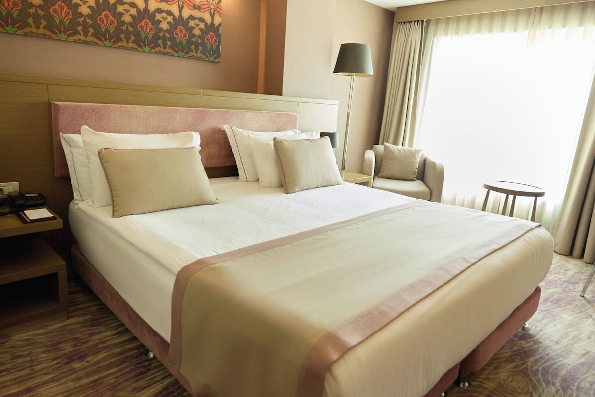 A hotel room with a large bed, a nightstand, a chair, a small table, and a lamp.