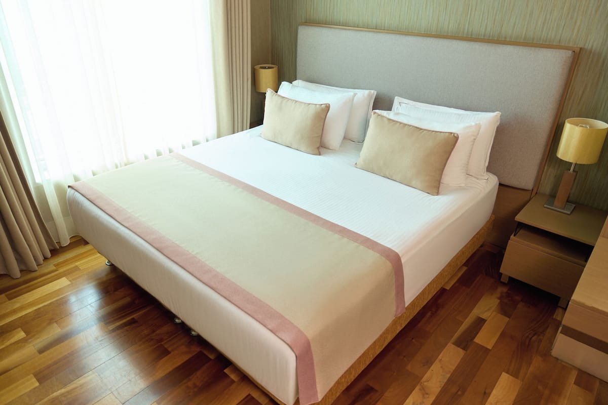 A neatly made bed with a pink accent, a wooden floor, and two bedside lamps.
