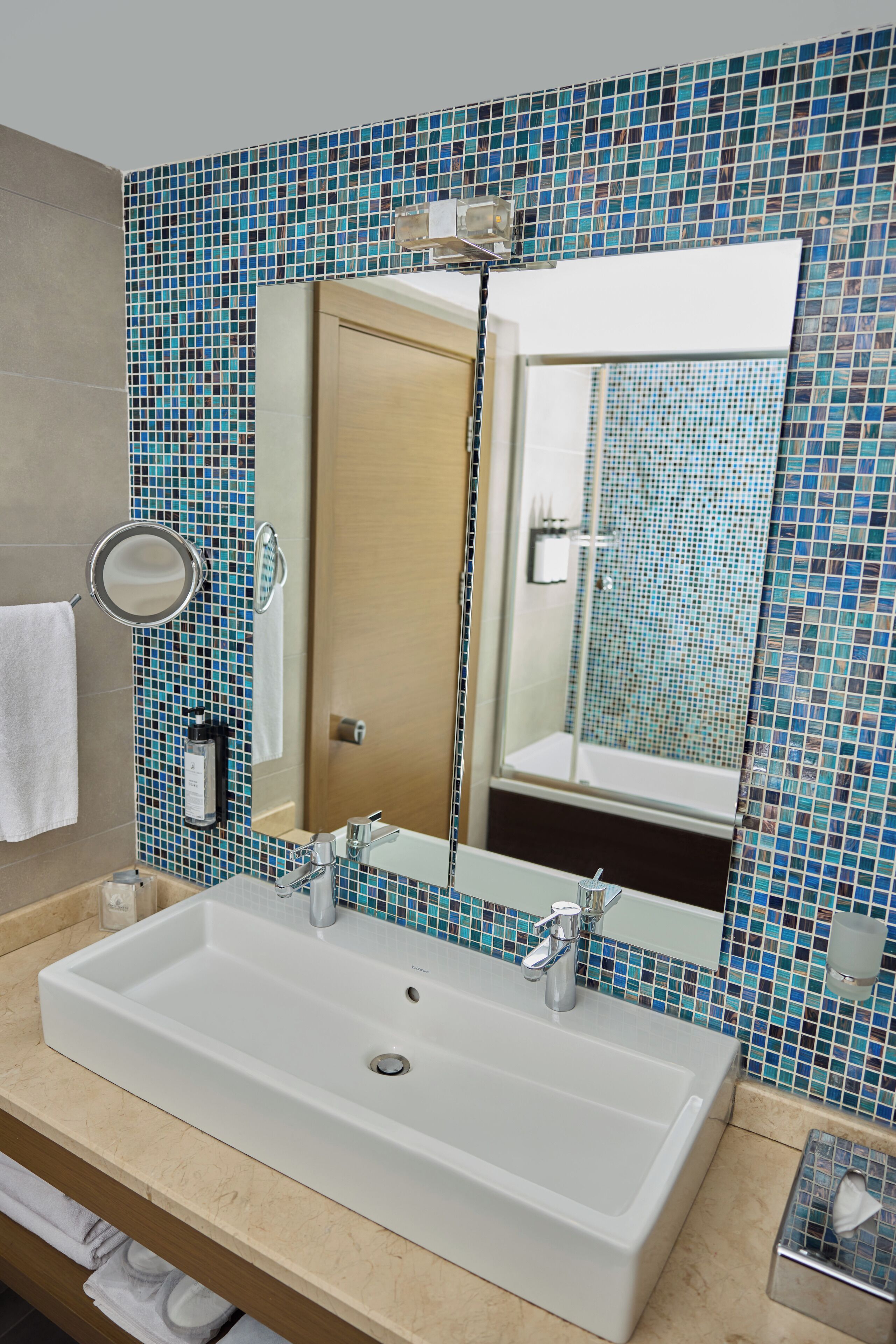 A bathroom with a large white sink, a mirror, and a blue mosaic tile wall.